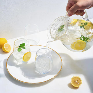A clear acrylic beverage pitcher with a lid, filled with a refreshing beverage adorned with lemon slices and ice cubes.