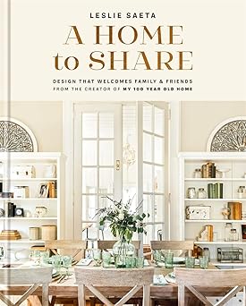 Cover of the book 'A Home to Share' by Leslie Saeta, featuring an image of a cozy dining room with a set table, bookshelves, and large windows. A Home to Share.