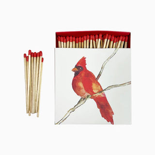 A box of matches with a printed illustration of a red cardinal bird on the cover, alongside a spread of matchsticks with red tips, anne neilson