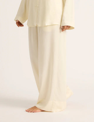 A pair of pearl beige wide leg sleep pants made from vegan silk, featuring a relaxed fit with side pockets and stitched front detailing.