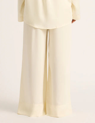 A pair of pearl beige wide leg sleep pants made from vegan silk, featuring a relaxed fit with side pockets and stitched front detailing.