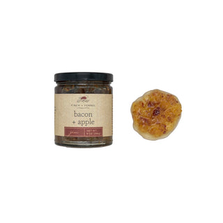 A jar of bacon and apple jam with the label showing the product name and a helping of the jam spread on a white surface, finch and fennel 