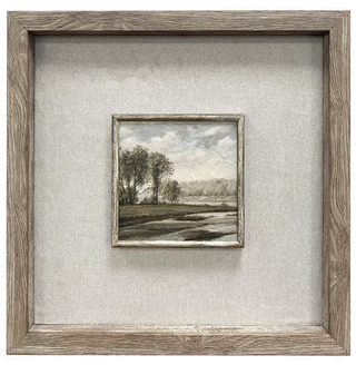 Barton Framed Wall Art Assorted
A square framed landscape art print with a rustic gray-brown wood frame and a textured light gray linen mat. The small central painting depicts a muted countryside scene with trees, hills, and a cloudy sky.