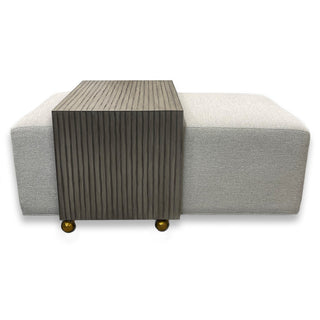 Burton James fabric ottoman in Alexandria Powder with brown accent waterfall table and wheels for movement.