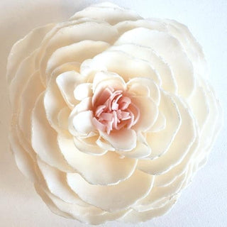 A white, floral-shaped soap made from hand-piecing goat's milk, shea butter, and coconut oil, with a pink center. Butterfly Kisses Petal Soap Flower.