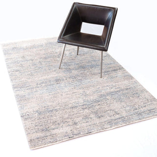 A rectangular area rug with a textured design featuring shades of grey and blue styled with a leather chair.