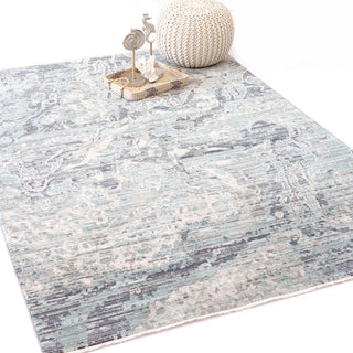 A rectangular area rug with a modern geometric pattern in shades of blue and gray styled with cream home decor.