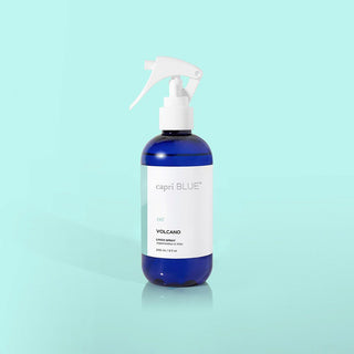 A blue bottle with a white spray nozzle labeled 'Capri Blue' and 'Volcano', on a blue background.
