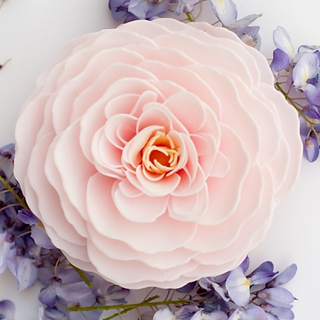 A large, pink rose petal soap arranged to form a flower, with smaller purple flowers around it on a white background. Cherry Blossom Heirloom Rose Petal Soap.