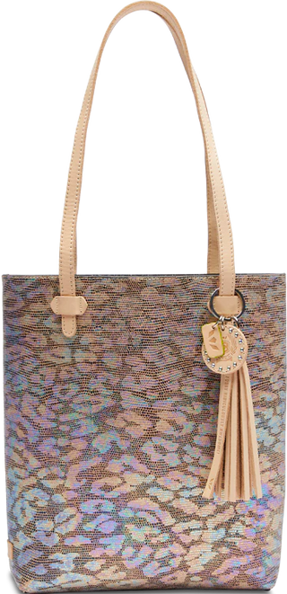 A textured leather tote bag with an iridescent jag print exterior, featuring a circular leather charm and tassel, and brown natural leather trim and handles.