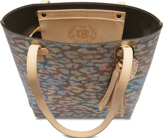 A textured leather tote bag with an iridescent jag print exterior, featuring a circular leather charm and tassel, and brown natural leather trim and handles.