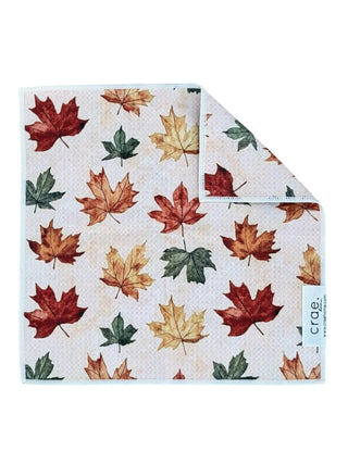 A square fabric cloth with an all-over autumn maple leaf print in red, orange, yellow, and green on a light cream background, Crae Crisp Morning: Double-Sided Washcloth