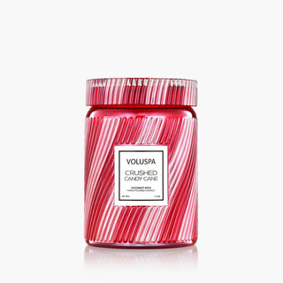 A Voluspa 'Crushed Candy Cane' coconut wax candle in a clear glass jar with a matching patterned lid, featuring diagonal red and white candy cane stripes and a white label in the center. Voluspa Crushed Candy Cane Large 18oz Candle