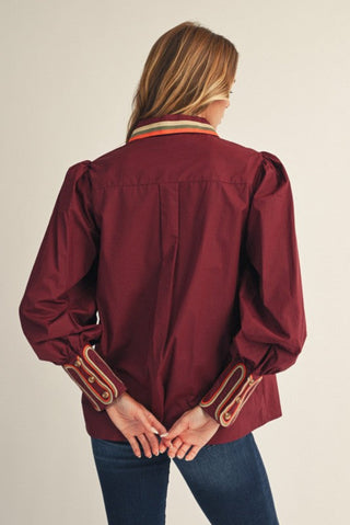 Person wearing a burgundy jacket with decorative cuffs on a plain background. Embroidery Accent Button Down Shirt in Burgundy