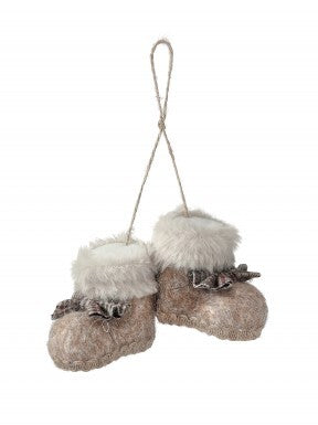 A pair of hanging boot-shaped ornaments in a rustic beige and brown faux fur style, with white faux fur trim and a small brown bow on each, suspended by a twine loop against a white background.