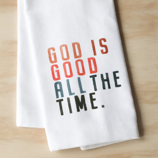 White towel with 'God is Good All the Time' text on a wooden surface