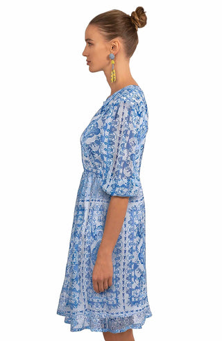 A woman wearing a blue Gretchen Scott crinkly dress with a geometric pattern and elbow-length sleeves.