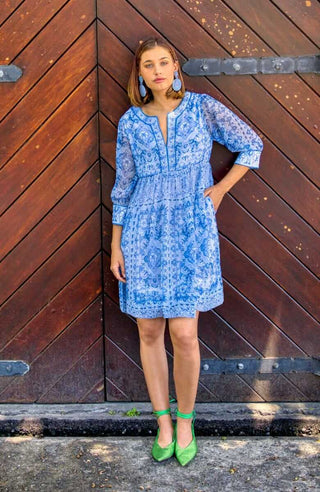 A woman wearing a blue Gretchen Scott crinkly dress with a geometric pattern and elbow-length sleeves.