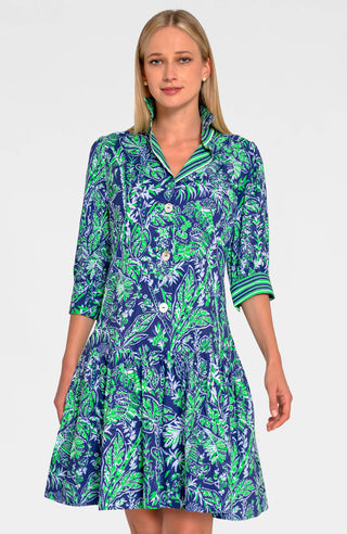 A woman wearing a navy dress with a green leaf pattern. The dress has long sleeves, a V-neck, and a flared skirt.