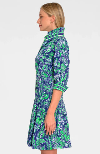A woman wearing a navy dress with a green leaf pattern. The dress has long sleeves, a V-neck, and a flared skirt.
