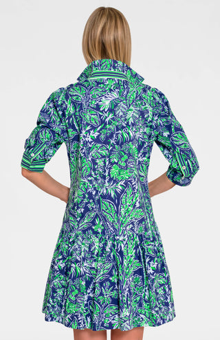 A woman wearing a navy dress with a green leaf pattern. The dress has long sleeves, a V-neck, and a flared skirt.