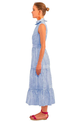 A model wearing a blue Gretchen Scott wash and wear hope midi/maxi dress with a double pleated collar, tiered banded gathered skirt, elasticized waist, side seam pockets, and coordinating inside back panel.