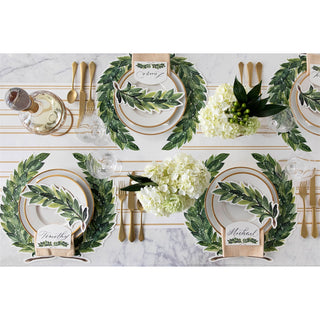 Elegant table setting with green leafy placemats, white plates, and gold cutlery on a marble surface.