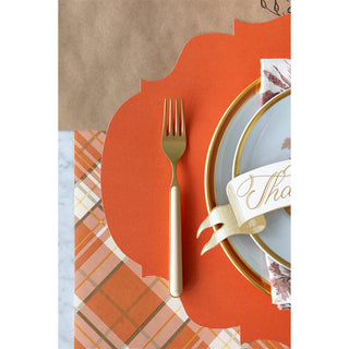 Thanksgiving table setting with a fork, plate, and decorative elements on an orange background.