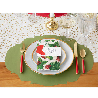 Christmas-themed place setting with holly design napkin and red cutlery on a gold polka dot table runner
