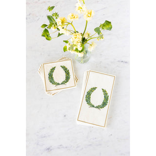 Set of napkins with green wreath designs on a marble surface with a small bouquet of flowers.
