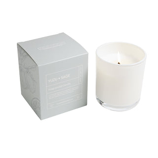 White candle in a glass container with a white box labeled 'Yuzu Sage' on a white background