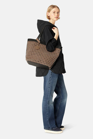 Woman holding a large brown perforated tote bag against a white background