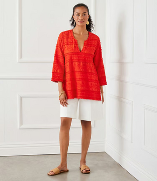 A woman wearing an orange tunic with 3/4 length sleeves and embroidery details.