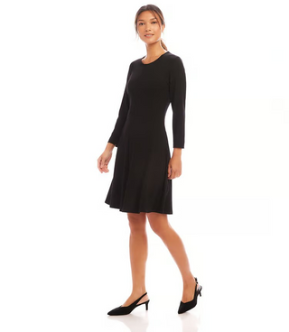 A woman standing in a studio setting, wearing a knee-length black dress with 3/4 sleeves, scoop neck, and fit and flare silhouette. 