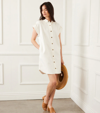 Woman wearing a white dress with buttons against a white paneled wall.