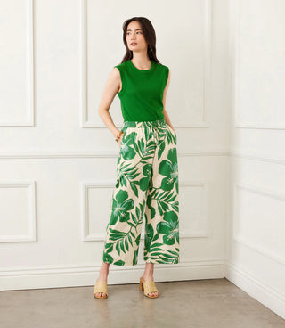 Woman wearing a green sleeveless top and leaf-patterned pants against a white wall.