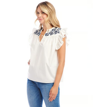 A woman wearing an off white top with navy blue embroidered ruffle sleeves and a split neck.