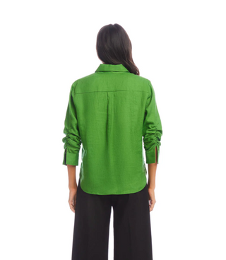 A woman wearing a green linen shirt with ruched sleeves, a collar, and front button closure. She has a front patch pocket and is paired with black pants.