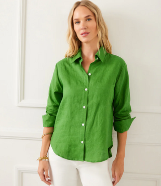 A woman wearing a green linen shirt with ruched sleeves, a collar, and front button closure. She has a front patch pocket and is paired with black pants.