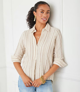 A woman wearing a beige and white metallic striped ruched sleeve shirt with a collar, paired with blue jeans.