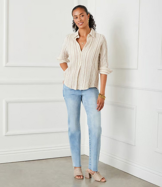 A woman wearing a beige and white metallic striped ruched sleeve shirt with a collar, paired with blue jeans.