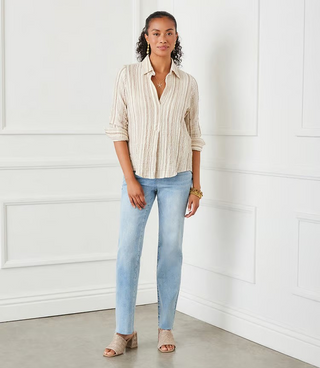 A woman wearing a beige and white metallic striped ruched sleeve shirt with a collar, paired with blue jeans.
