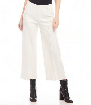 A pair of off white pintuck wide leg pants with an elastic waistband, displayed on a model with black boots.