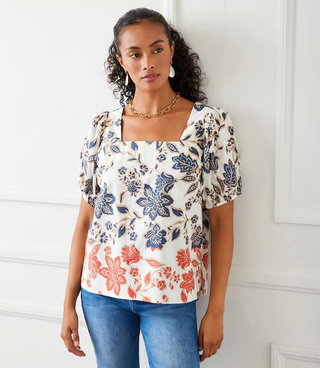 A woman wearing a square neck top with puff sleeves and a navy and orange print, paired with jeans.