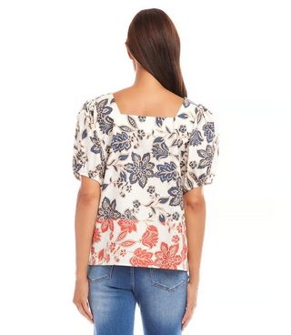 A woman wearing a square neck top with puff sleeves and a navy and orange print, paired with jeans.