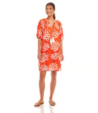 A woman wearing an orange knee-length cotton dress with a coral reef print, puff sleeves, and a split neckline.