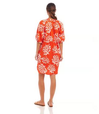A woman wearing an orange knee-length cotton dress with a coral reef print, puff sleeves, and a split neckline.