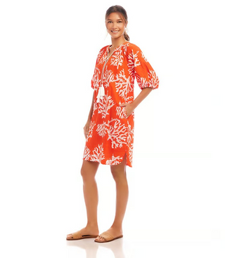 A woman wearing an orange knee-length cotton dress with a coral reef print, puff sleeves, and a split neckline.