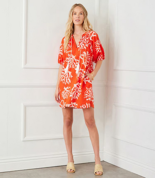 A woman wearing an orange knee-length cotton dress with a coral reef print, puff sleeves, and a split neckline.