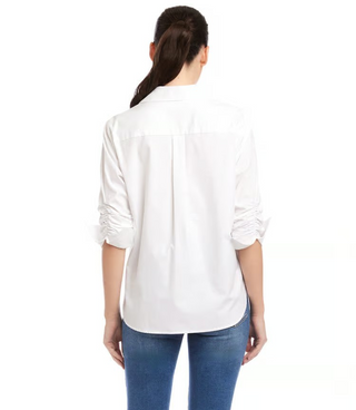 A woman wearing a white Karen Kane button-up shirt with rolled sleeves and a collar, paired with blue jeans.